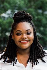 A beautiful young, Black american woman holds a warm smile in a headshot photo.